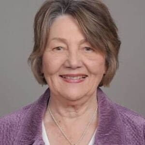 Older woman smiling in purple jacket.