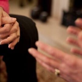 A group of people sitting in a circle with their hands clasped.